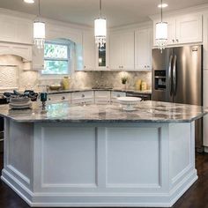 a large kitchen with white cabinets and marble counter tops, an island in the middle