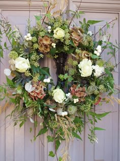 a wreath with white flowers and green leaves hanging on the front door to decorate it