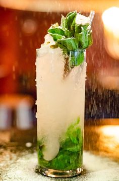 a tall glass filled with ice and green leafy drink garnished with mint