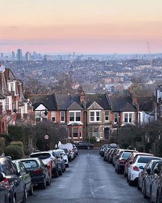 many cars parked on the street in front of houses with city skyline in the background