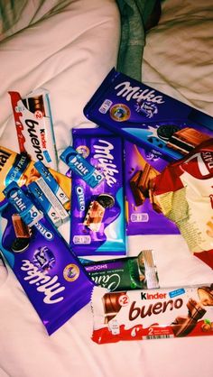 a pile of chocolate bars and candy on a bed with someone's feet in the background