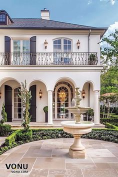 A beautiful Mediterranean-style villa with arched doorways, wrought-iron balconies, and a central courtyard featuring a classic fountain, surrounded by lush greenery, embodying elegance and charm. Villa With Courtyard, Modern French House, French Mediterranean Home, Classic Villa Exterior, Courtyard Fountain