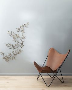 a chair sitting in front of a white wall with gold leaves on it and a wooden floor