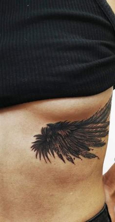 a woman's stomach with a black tattoo on her belly and an angel wing