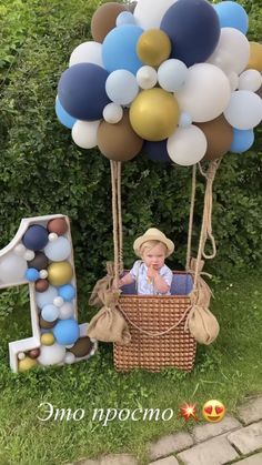 a baby in a basket with balloons and the number one on it's side