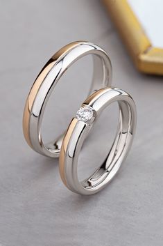 two wedding rings sitting on top of each other with a diamond in the middle,