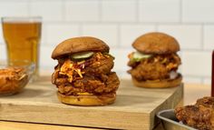 three fried chicken burgers with pickles and cole slaw on a cutting board