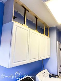 a washer and dryer in a blue room with white cabinets under construction on the wall