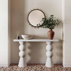 a white table with a mirror on the wall and some plants in a vase next to it