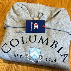 a grey sweatshirt with the word columbia on it sitting on a wooden floor next to a tag