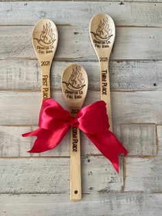 two wooden spoons with red ribbon tied around them on top of a wood table