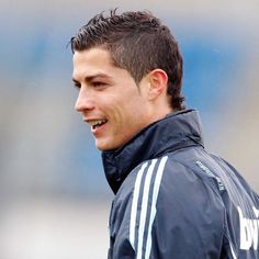 a young man in a black jacket smiles at the camera while standing on a soccer field