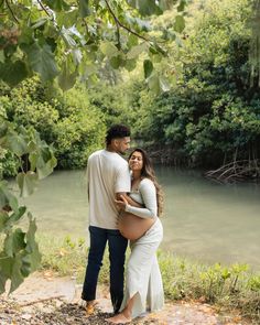 a pregnant couple standing next to each other in front of a river