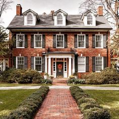 a large brick house with white trim and black shutters on the front door is shown