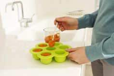 a person standing in front of a sink pouring something into a bowl with oranges on it