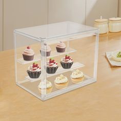 four cupcakes in a glass case on a table