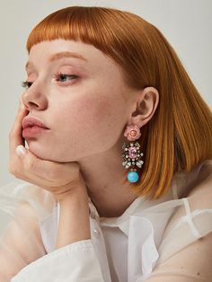 a woman with red hair wearing earrings and a white shirt is looking off to the side