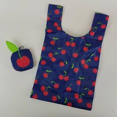 a blue bag with red cherries on it next to a small apple and green leaf