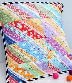 a multicolored pillow sitting on top of a white table next to pom poms