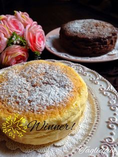 two plates with cakes on them and pink flowers in the background, one has powdered sugar on top