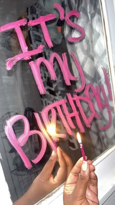 a person holding a lit candle in front of a window that says, it's my birthday