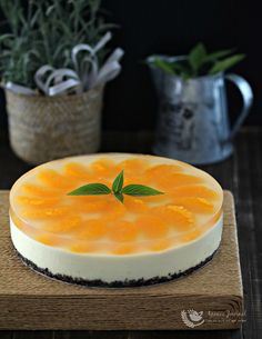 a cheesecake with orange sauce and green leaf decoration on top, sitting on a wooden board