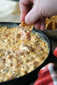 a hand dipping a tortilla chip into a skillet