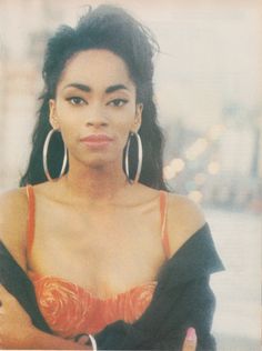 a woman with large hoop earrings and an orange bra posing for a photo in front of a city street