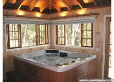 a large hot tub in the middle of a room with wood paneling and windows