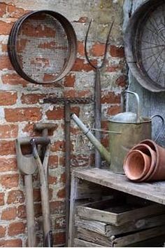 an old wooden table topped with lots of pots and pans next to a brick wall