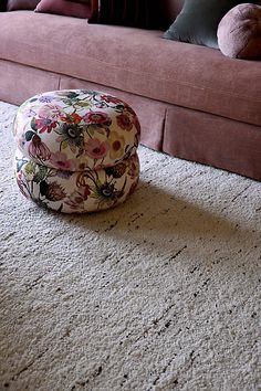 a living room with a pink couch, ottoman and flowered hat on the floor