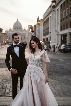 a man and woman in formal wear walking down the street with their arms up to each other