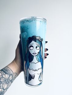 a tattooed hand holding up a blue drink with a drawing on it's side