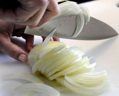 a person cutting onions with a knife on a counter top in front of the onion