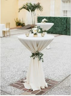 a white table topped with flowers and greenery on top of a stone floor next to two vases