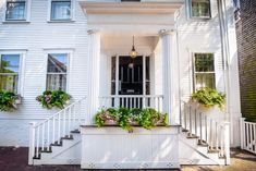 a white house with flowers in the window boxes on the front porch and stairs leading up to the door