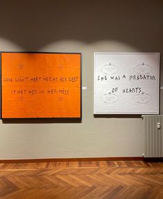 two orange and white posters on the wall in an empty room with wood floors,