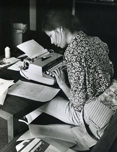 a woman sitting at a desk with papers and a typewriter in front of her