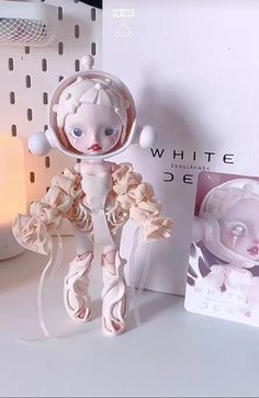 a white doll sitting on top of a table next to a box