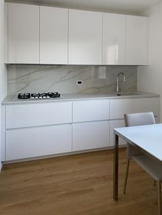 an empty kitchen with white cabinets and wood flooring, along with a dining table in the foreground