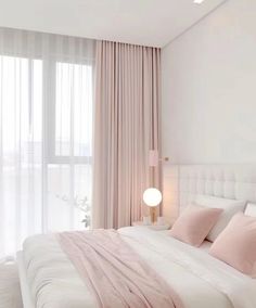 a white bed with pink pillows and blankets in a bedroom next to a large window