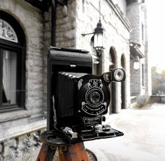 an old camera sitting on top of a wooden tripod in front of a building