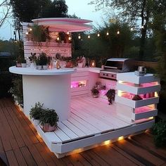 an outdoor kitchen is lit up with pink lights and potted plants on the deck