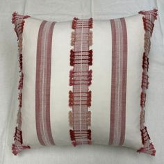 a red and white striped pillow with tassels on the bottom, sitting on a bed