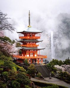 a tall pagoda with stairs leading up to it in the middle of trees and flowers