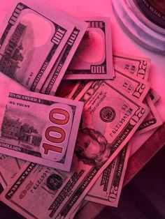 several stacks of one hundred dollar bills sitting on top of each other in front of a pink background