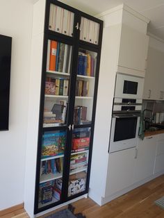 a book case with many books in it next to a wall mounted oven and microwave