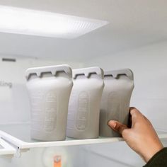 three plastic bottles are on a shelf in a store, being held by a person