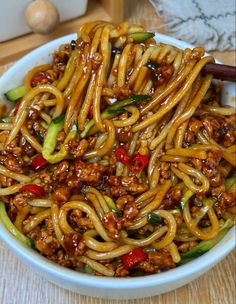 a white bowl filled with noodles, meat and veggies next to chopsticks