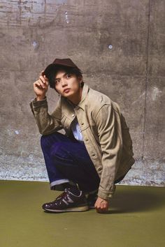 a young man squatting on the ground with his hand in his hat and shoes